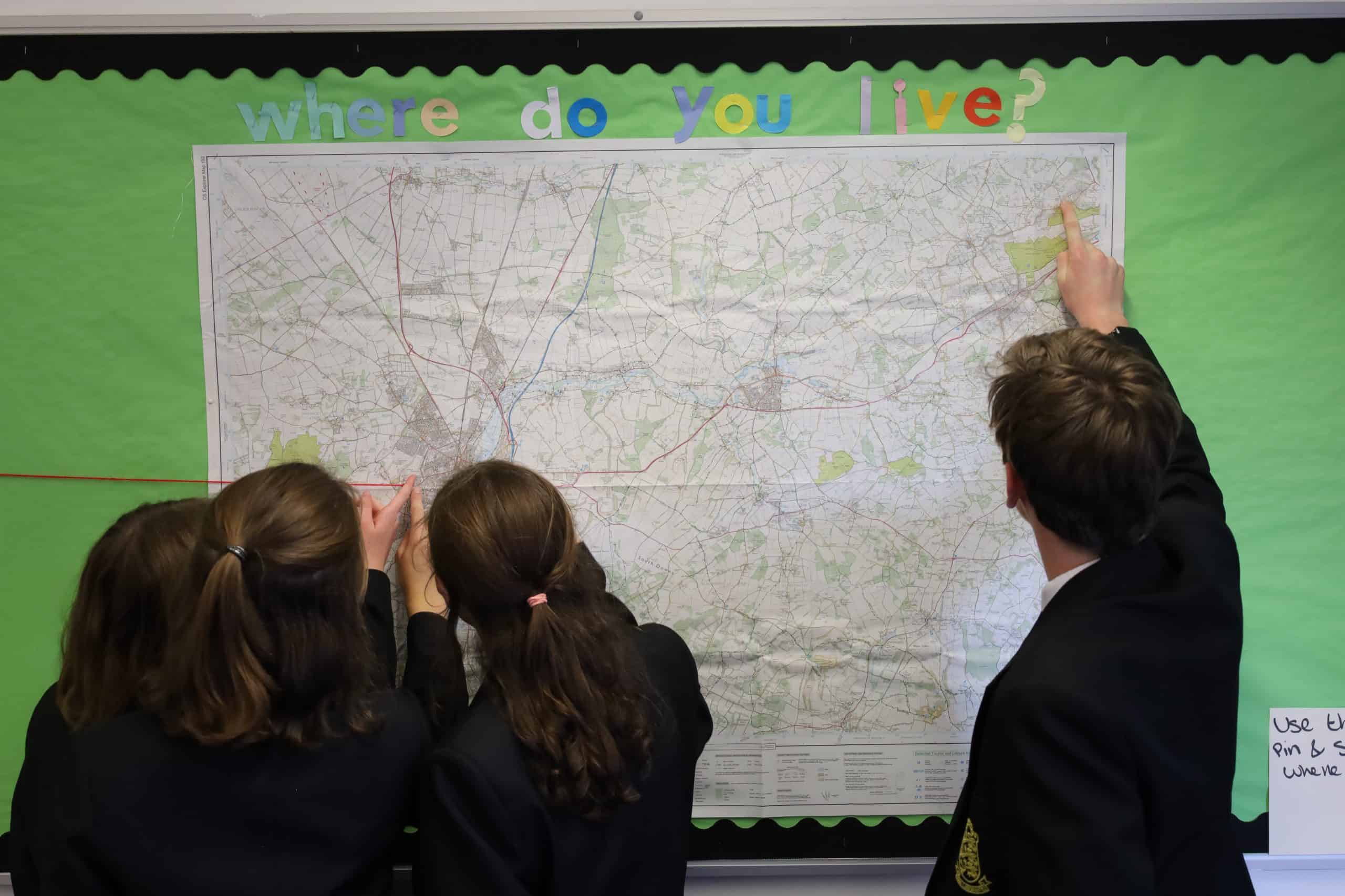 Picture shows 4 children in Kings' School uniform pointing to different places on a map which is displayed on a wall