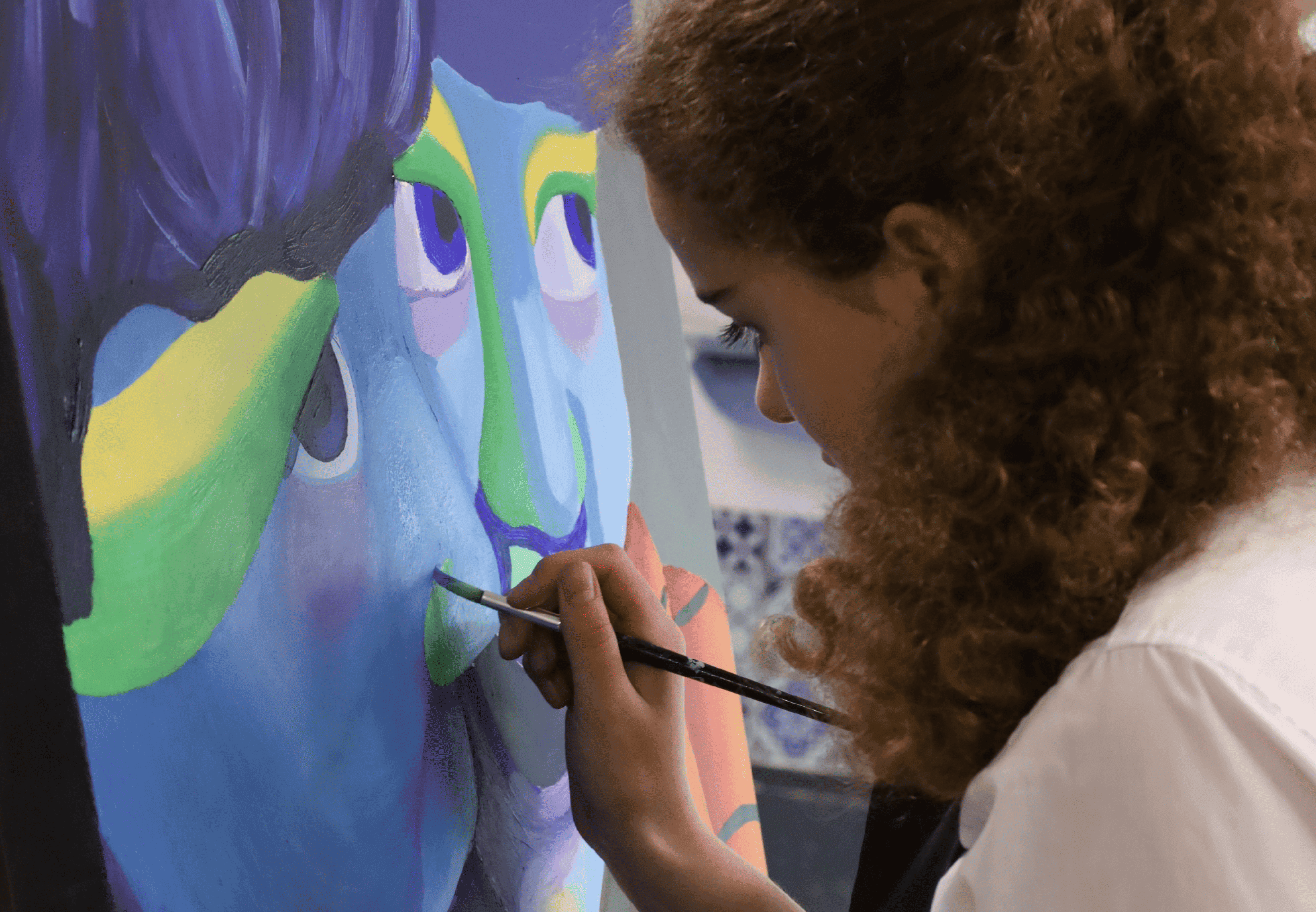 Young girl painting colourful abstract portrait at Kings School arts programme.