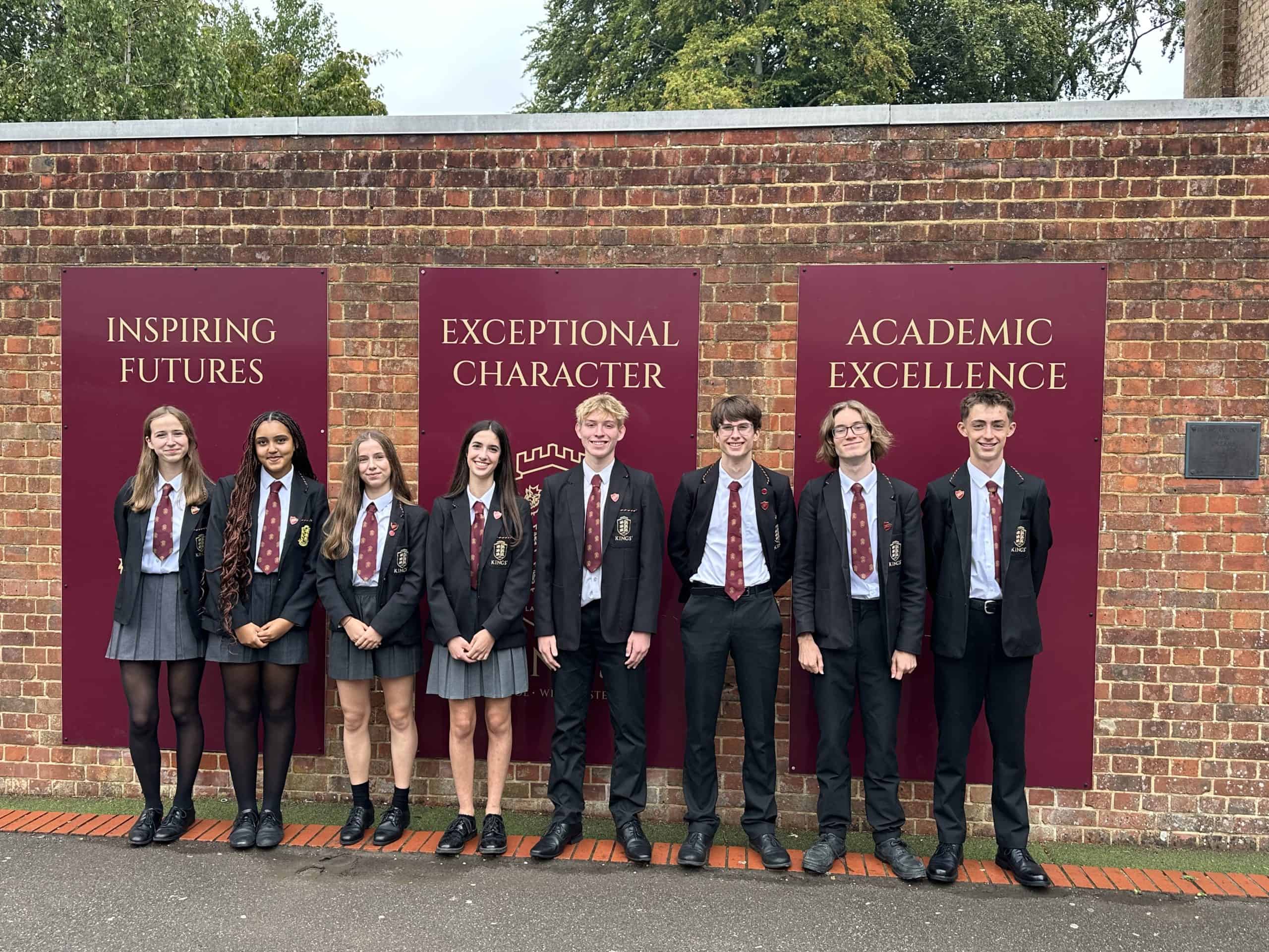 Group of students in school uniform standing in front of Kings School banners.